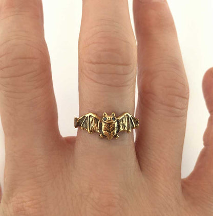 14k Gold bat ring on a person's finger with a plain background