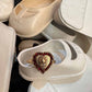 White baby shoes with a heart-shaped gold ring on top, surrounded by more white shoes.