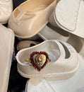 White baby shoes with a heart-shaped gold ring on top, surrounded by more white shoes.