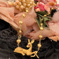 A gold-toned necklace featuring a deer pendant and heart-shaped beads, styled on a black lace surface with pink fabric and faux flowers in the background.