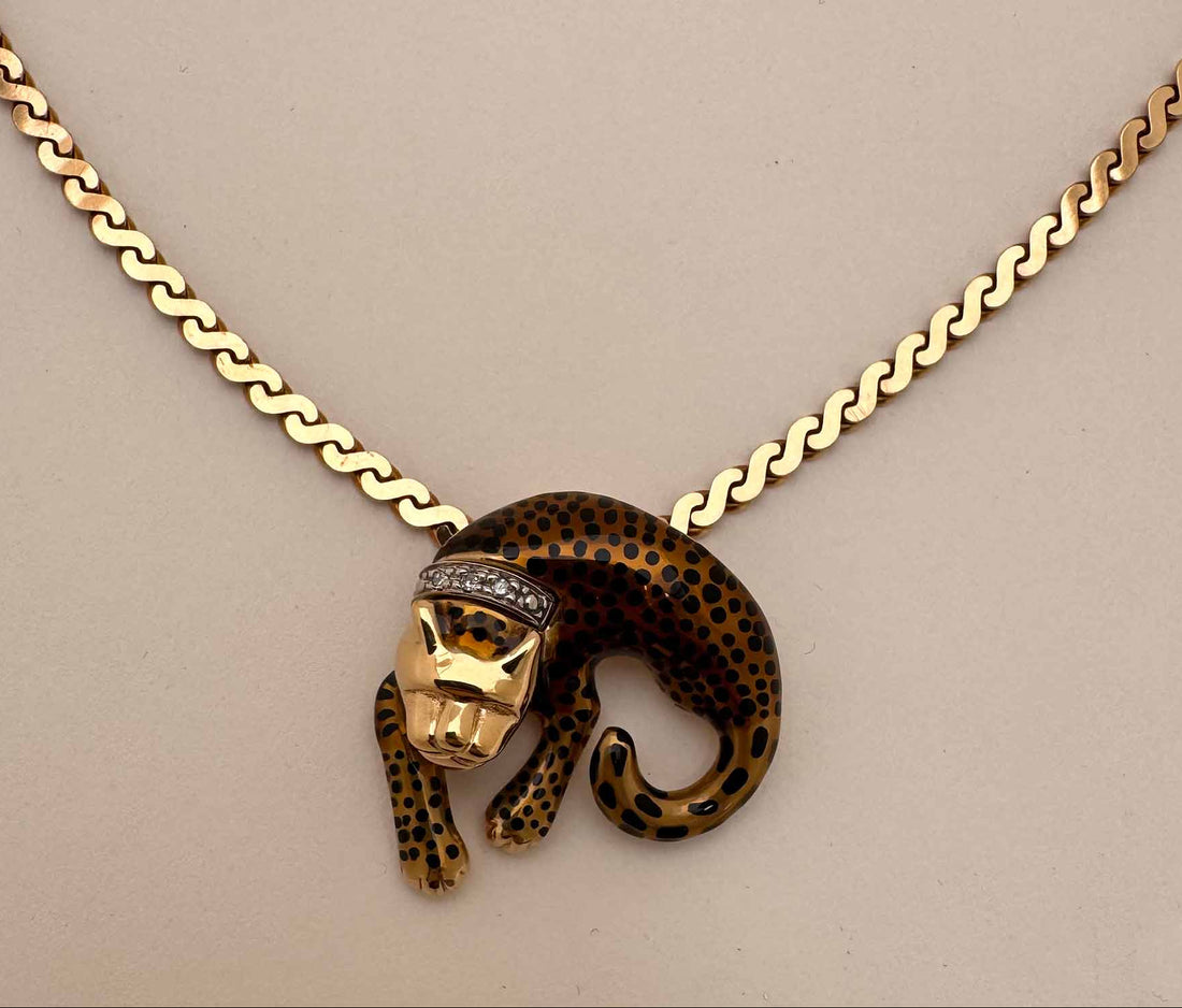 A gold chain necklace featuring a leopard pendant with a gold and black spotted pattern and a small diamond crown, displayed on a neutral beige background.