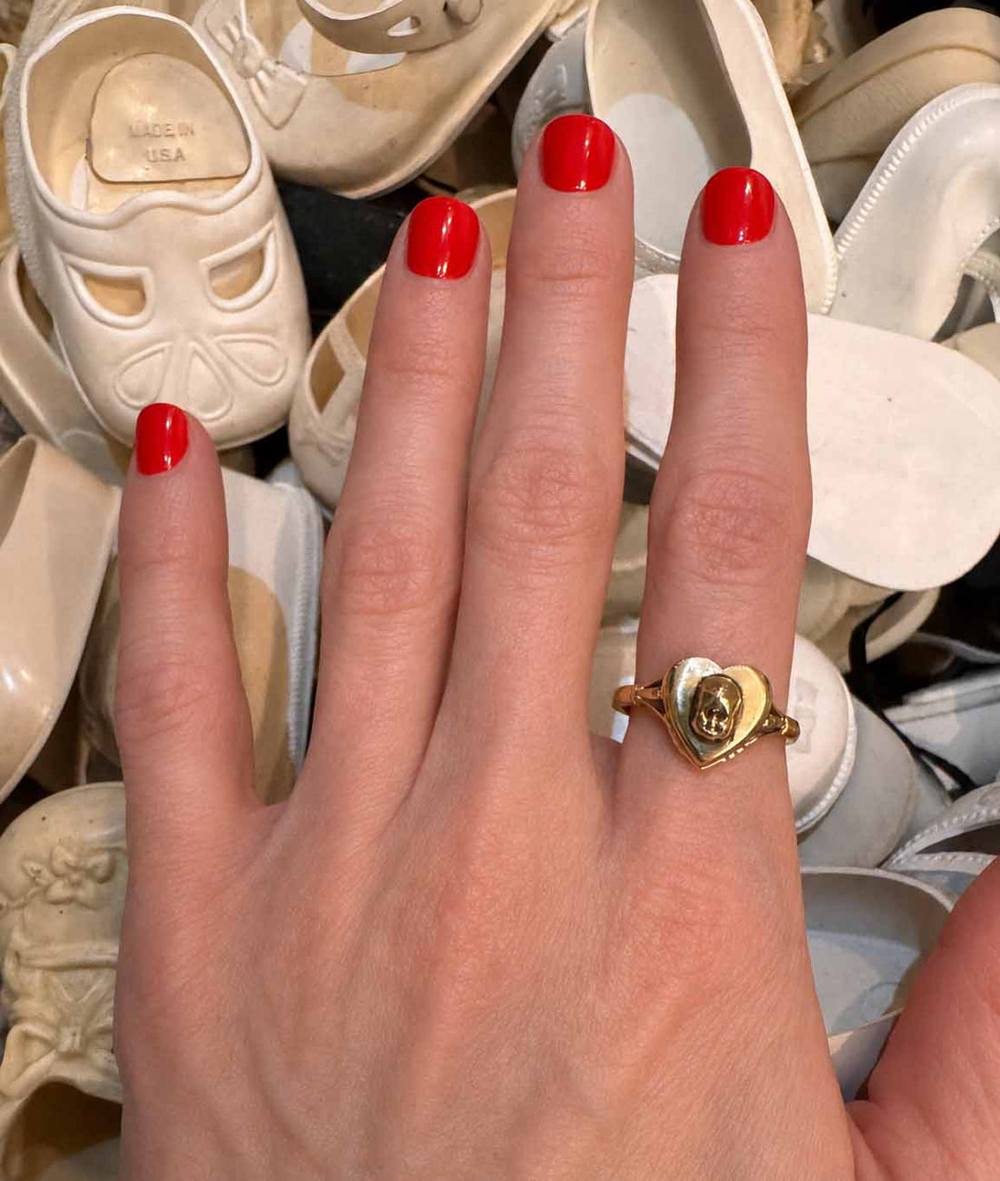 One of a kind 14K gold vintage heart ring with hand sculpted baby head by Anomaly Relic, photographed among antique baby shoes on a young woman's hand