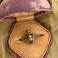 14K Gold panther and baby head ring  handmade by anomaly relic in nyc with green gemstone in a purple velvet box on a yellow fabric background