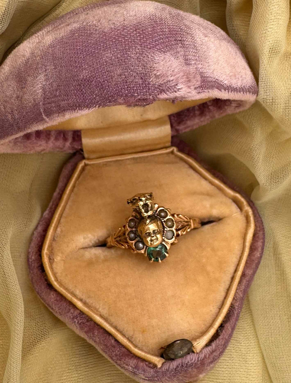 14K Gold panther and baby head ring  handmade by anomaly relic in nyc with green gemstone in a purple velvet box on a yellow fabric background